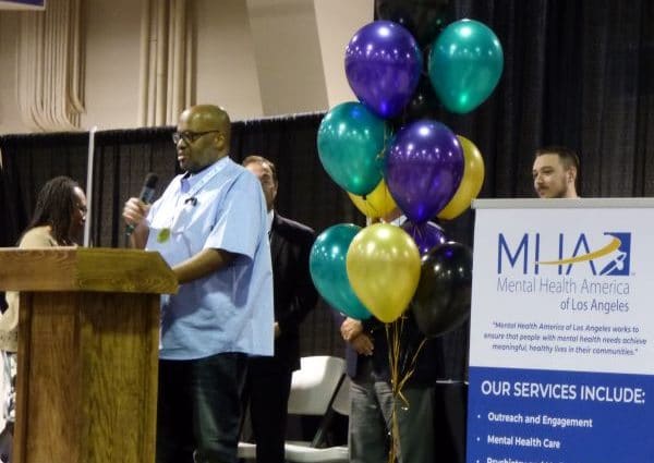 Man at podium speaking into microphone with balloons next to him