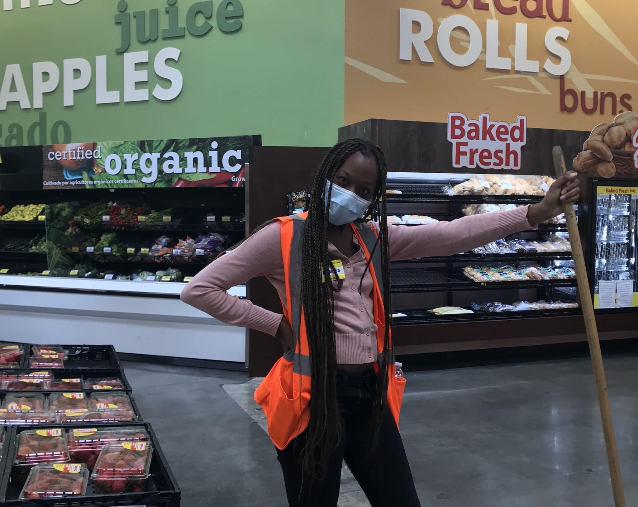 Young woman in grocery store wearing a mask and holding a broom