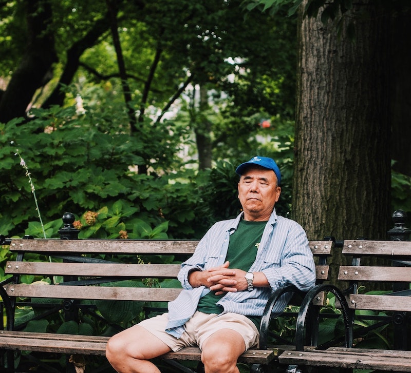 Man in shorts sitting on a park bench with his eyes closed