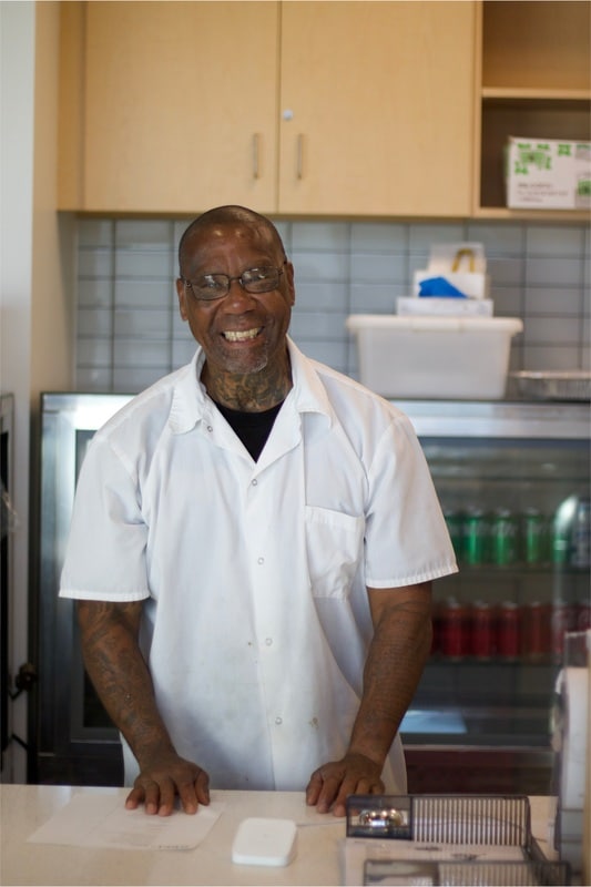 Man in chef jacket smiling and standing in bakery