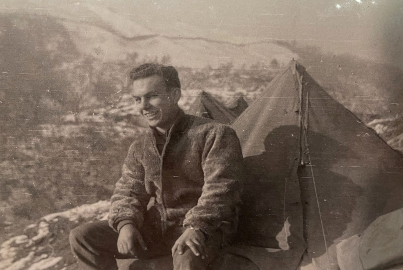 Young male soldier sitting near a tent on a mountain during World War II