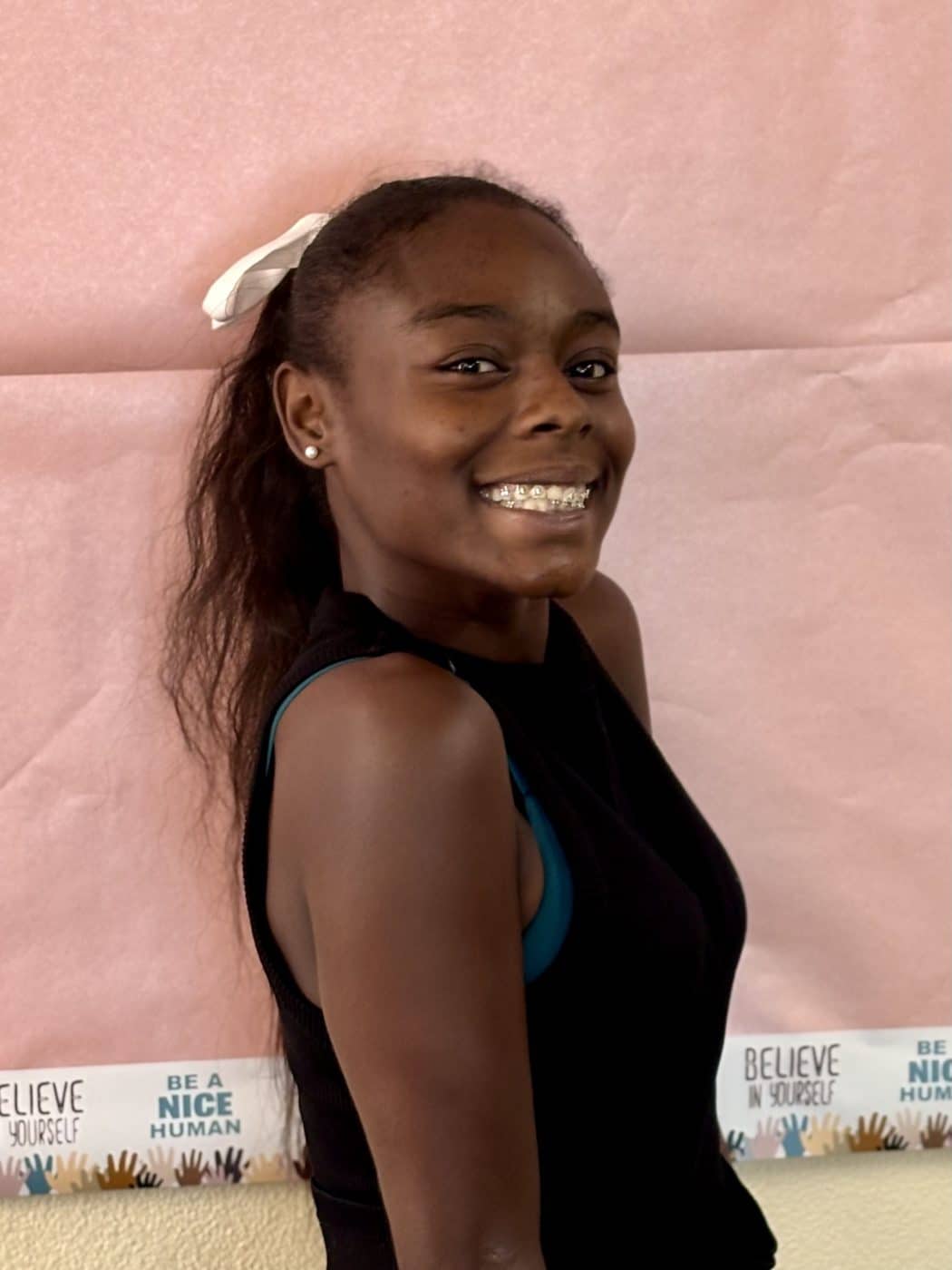 Young woman in black tank top smiling in front of pink backdrop