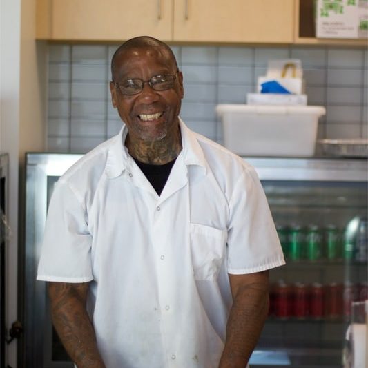 Gerald S Man in chef jacket smiling and standing in bakery